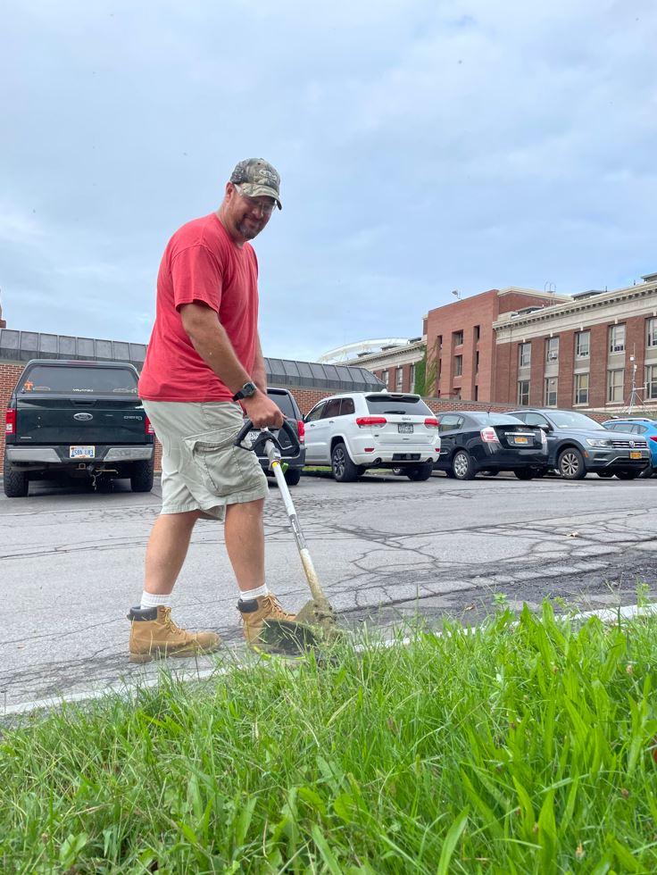 grounds crew member trims with electric string trimmer