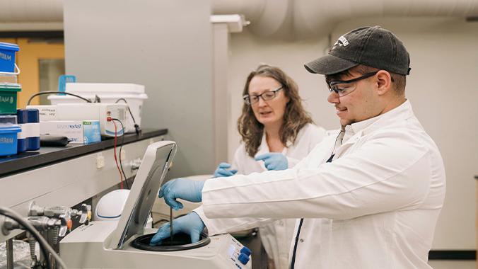 Faculty supervising a student using a centrifuge for biochemical samples.